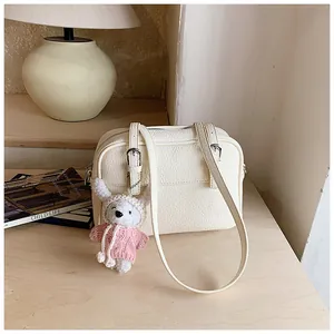 Detail of cream lychee texture crossbody bag with cute white plush bunny charm accessory