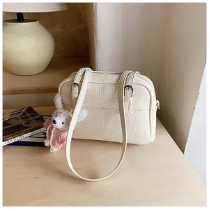 Detail of lychee textured cream crossbody bag with a cute white rabbit plush charm