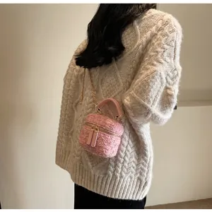Detailansicht der rosa Tweed-Minibox-Tasche mit Goldkette auf cremefarbenem Strick