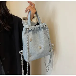Détail du sac à main en denim bleu clair avec œillets métalliques et bandoulière chaîne
