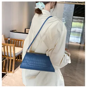 Blaue Baguette-Tasche mit Krokoprägung an der Schulter eines Models in Luxusumgebung
