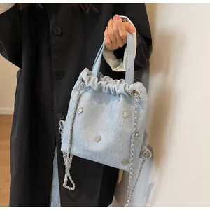 Détail du sac seau en denim bleu clair avec des rivets métalliques en forme de cœur