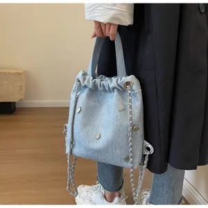 Détail du sac seau en jean bleu clair avec rivets en cœur et chaîne porté par un mannequin