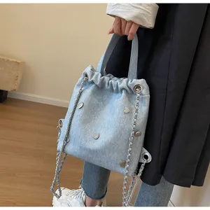 Détail du sac seau en jean bleu clair avec rivets en cœur et bandoulière chaîne