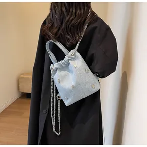 Détail du sac seau en denim avec clous argentés et breloque coeur porté par un mannequin