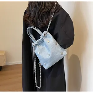 Détail du sac seau en denim bleu clair avec rivets argentés et chaîne sur un mannequin