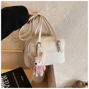 Detail of off-white lychee grain leather crossbody bag with cute plush bear charm