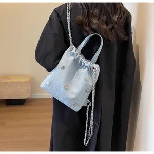 Détail du sac seau en denim bleu clair avec rivets cœurs argentés et bandoulière chaîne