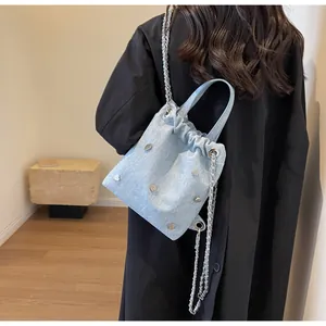 Détail du sac seau en denim bleu clair avec clous argentés porté par un mannequin