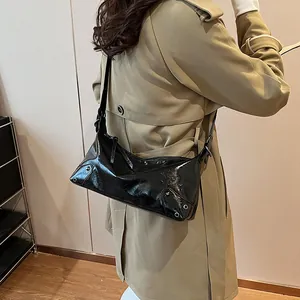 Sac fourre-tout noir verni demi-lune avec clous argentés porté sur un trench-coat kaki