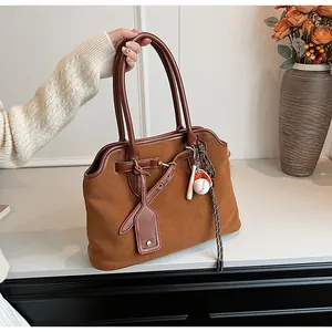 Detailed close-up of brown suede hobo bag with leather straps and sports charms on table