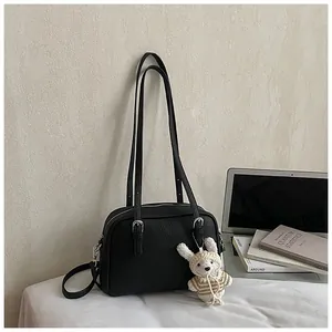 Detailed view of black litchi texture square bag with a cute knit rabbit charm on desktop