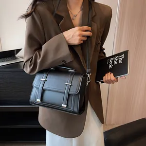 Detail of a black textured leather crossbody bag with silver buckles and handle strap