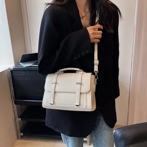 Detail of off-white leather handbag with silver buckles shown in an office setting