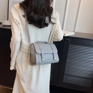 Light grey crossbody satchel with buckle straps shown in a lifestyle street setting