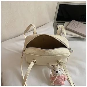 Detail view of cream lychee texture crossbody bag with cute sheep charm on white desk