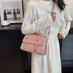 Detail of pink crossbody bag with silver buckles worn with a textured white dress