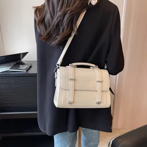Detailed view of cream PU leather crossbody bag with top handle worn on black blazer