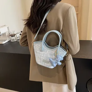 Sac seau bleu clair tressé élégant avec breloque ours porté par un mannequin en blazer