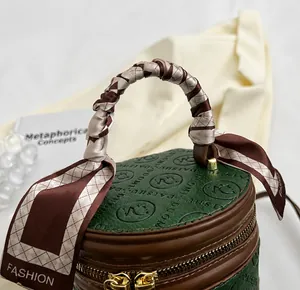 Detail of green cylinder handbag with embossed logo and decorative checkered silk scarf handle