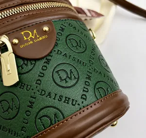Detail of green embossed leather crossbody bag with brown trim and gold hardware