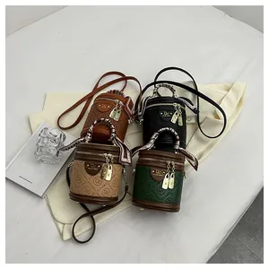 Detail of a cylindrical bucket bag with embossed logo, silk scarf handle and shoulder strap