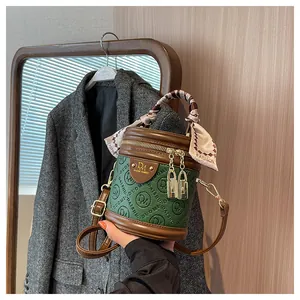 Detail of green cylinder bucket bag with embossed logo texture and silk scarf handle