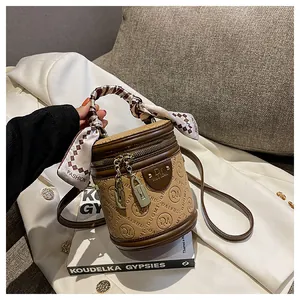 Detail of retro cylindrical PU leather crossbody bag with embossed logo and silk scarf handle