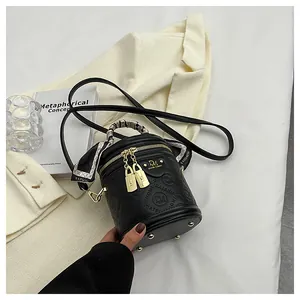Detail of black cylindrical PU leather crossbody bag with brand embossing and silk scarf handle