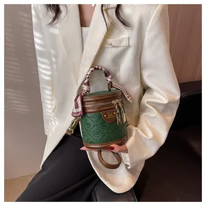 Detail of dark green mini barrel bag with silk scarf handle and golden metal hardware
