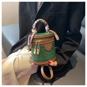 Detail of green embossed cylinder bag with brown trim and decorative silk handle scarf