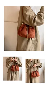 Detail view of rust-red suede bucket bag with drawstring closure and golden chain tassel