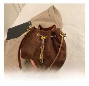 Detail showing the brown suede bucket bag with gold chain drawstring and metal hardware
