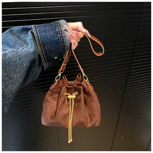 Detail of brown suede drawstring bucket bag with gold chain strap held by a model