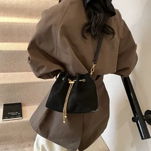 Minimalist black suede bucket bag with gold chain drawstring and adjustable strap