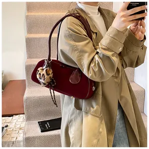 Detail of dark red velvet underarm bag with leopard heart charm in autumn city scene