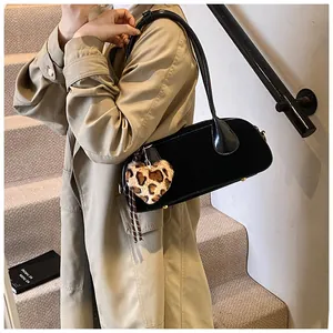 Detail view of a black glossy underarm bag with leopard heart charm on a beige trench coat