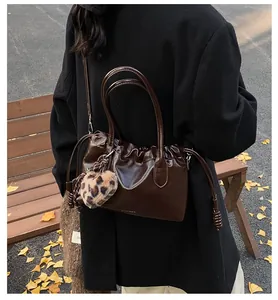 Détail du sac plissé marron foncé avec breloque cœur léopard dans un décor d'automne