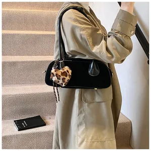 Close-up of black patent leather shoulder bag with leopard heart plush charm pendant