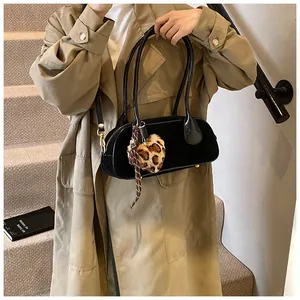 Detail of black matte bowling bag with leopard heart charm worn over a khaki trench coat