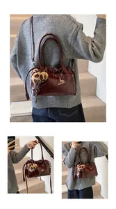 Sac à main plissé en cuir verni bordeaux avec pompon léopard sur escalier