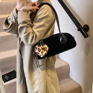 Glossy black underarm bag with a leopard print heart charm shown in a street style shot
