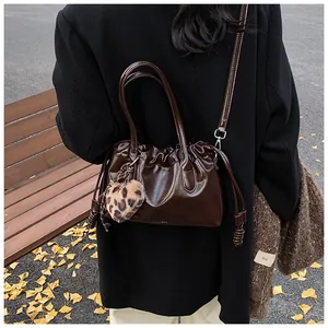 Détail d'un sac à main marron foncé en cuir brillant avec design plissé et bijou léopard