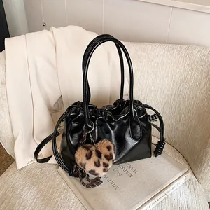 Sac à main noir plissé brillant avec breloque cœur léopard sur un canapé beige chic