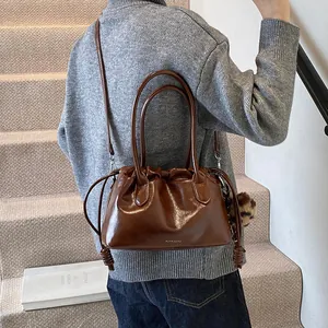 Sac à main plissé en cuir marron brillant avec pompon léopard sur un escalier minimaliste