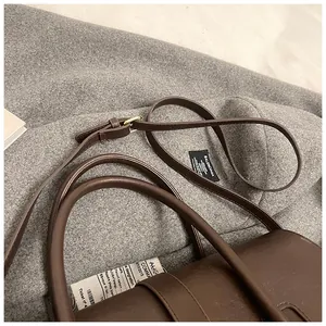 Detalle de bolso tote de cuero marrón oscuro con hebilla dorada sobre fondo de tela suave