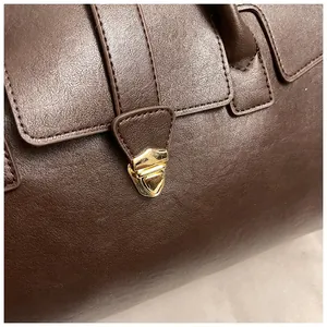 Detalle del bolso tote marrón oscuro con textura de cuero y cierre de metal dorado