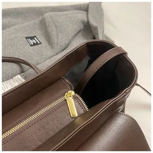 Detalle de bolso tote marrón oscuro con cremallera dorada y forro interior de tela negra