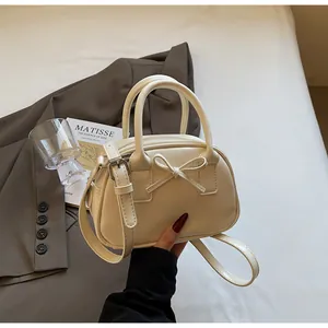 Detail of cream white leather handbag with 3D bow design and slim shoulder strap