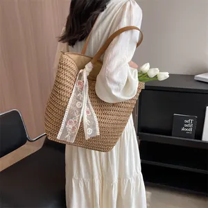 Detail of woven straw tote bag featuring white lace ribbon with pink floral embroidery